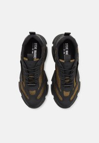 Zapatillas deportivas negras y doradas con parte superior de malla y acentos texturizados, suela de goma gruesa y cordones planos. Estilo: Steve Madden.