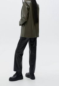 Blazer en cuir vert olive associé à un pantalon cargo en cuir noir et des bottes noires à lacets, avec une semelle épaisse et plusieurs poches.