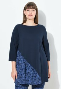 Top blu navy con un pannello diagonale a fantasia floreale. Presenta maniche a tre quarti e scollatura tonda, realizzato in tessuto morbido.
