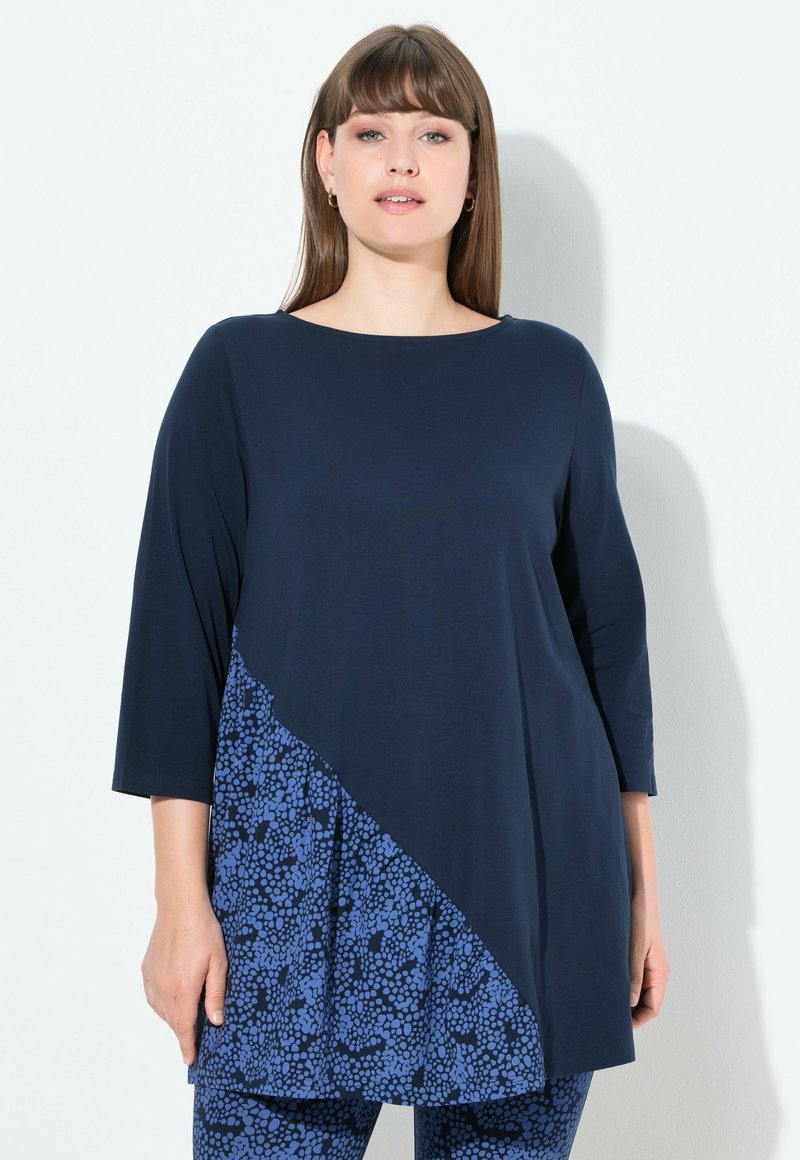 Top blu navy con un pannello diagonale a fantasia floreale. Presenta maniche a tre quarti e scollatura tonda, realizzato in tessuto morbido.