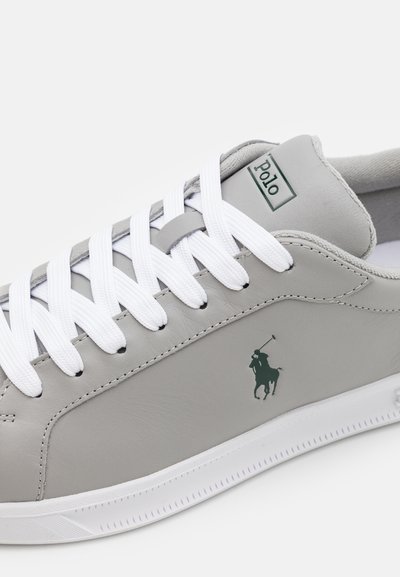 Sapatilha de couro cinza com atacadores brancos, apresentando um logo verde e um design texturizado subtil. A sola é branca com um padrão riscado.