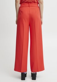 Red wide-leg trousers made from a smooth fabric, featuring a high waist, pleats, and a tailored fit. Worn with black platform shoes.