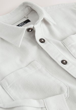 Lichtgrijs denim overhemd met een puntige kraag, donkere knopen en een enkele borstzak. De stof toont subtiele textuur en stiksel details.