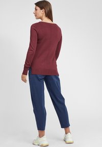 Maglione bordeaux a maniche lunghe con scollatura rotonda e spacchi laterali, abbinato a pantaloni blu navy larghi e scarpe da ginnastica chiare. Texture liscia.