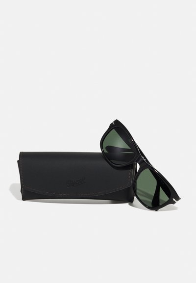 Óculos de sol Persol pretos com lentes verdes, apresentando um design de armação elegante e detalhes em prata, exibidos ao lado de uma caixa de couro preta.