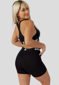 Čierny atletický outfit so športovou podprsenkou s prekríženými ramienkami a priliehavými šortkami s elastickým pásom a akcentami loga. Hladká, elastická látka.