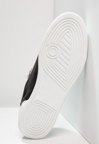 Černá bota s texturovaným svrškem, která má bílou gumovou podrážku. Viditelný vzor pro trakci na podrážce a metalický akcent na boku.