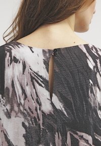 Krótki rękaw, czarno-różowy top z abstrakcyjnym wzorem, z wycięciem na plecach i dwoma czarnymi guzikami do zapinania, wykonany z miękkiej tkaniny.