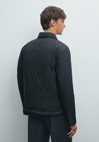 Black, padded jacket with a collar, featuring a smooth texture, simple design, and visible stitching. Designed for a relaxed fit.