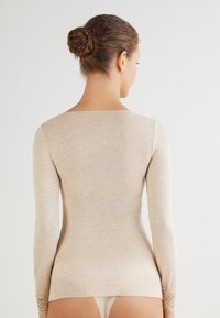 Beige långärmad topp i mjukt material, med fyrkantig halsringning och spetsdetaljer på ärmarna. Slät textur genom hela plagget.