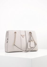 Sac à main gris clair avec un design matelassé, des accents en chaîne argentée et une étiquette de logo. Présente une forme structurée et deux anses supérieures.