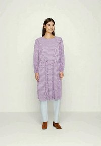 Vestido roxo de manga longa com cintura franzida, apresentando um padrão de bolinhas. Combinado com calças azuis claras e botas de tornozelo castanhas.