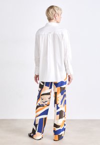 White button-up shirt with a back pleat, paired with wide-leg pants featuring orange, blue, and beige geometric patterns. Smooth texture, relaxed fit.
