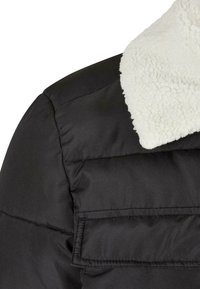 Sort pufferjakke med krave i faux fur. Har quiltet tekstur og vandret syninger. Inkluderer en klaplomme på siden.