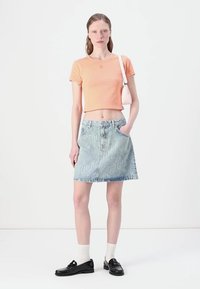 T-shirt cropped orange clair, mini-jupe en denim avec imprimé logo blanc, mocassins noirs et chaussettes blanches ; style simple et décontracté.