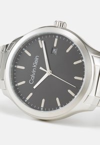 Reloj de acero inoxidable con esfera gris oscuro, marcadores de hora plateados, visualización de la fecha a las 3 en punto y un acabado pulido en la caja y la correa.