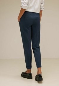 Námořnické kalhoty s tapered střihem, s hladkou texturou a manžetami na kotnících, v kombinaci s lesklými černými mokasíny.