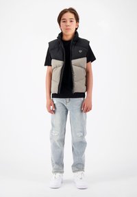 Gestepptes Weste in Schwarz und Grau, mit hohem Kragen und Reißverschluss, getragen über einem schwarzen T-Shirt, kombiniert mit hellen zerstörten Jeans und weißen Sneakers.