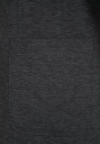 Tela de color gris oscuro con un acabado tejido texturizado y un bolsillo frontal prominente. El material parece suave y duradero.