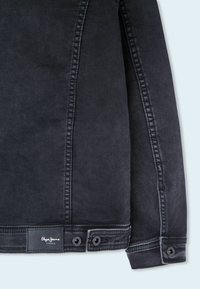 Black denim jacket with a smooth texture, featuring a buttoned cuff and a small logo patch near the hem. Structured design with visible seams.