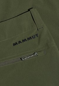Olivenfarvet stof med en glat tekstur præsenterer et synligt sort "MAMMUT" logo. Indeholder en lynlåslomme med en matchende træksnor.