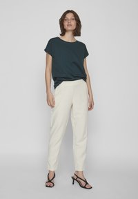 Dark teal short-sleeve t-shirt with a relaxed fit, paired with cream tapered pants. Model wears black strappy heels.