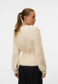 Krämfärgad stickad tröja med ribbat mönster, vida ärmar och en figurnära midja. Mjuk, något fluffig material med vertikala ränder.