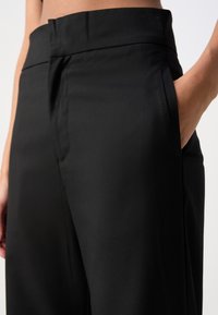 Pantalones negros con un tejido liso y brillante, cintura entallada, bolsillos laterales y corte de pierna recta para una silueta limpia.