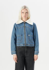 Világoskék farmerdzseki krém színű bundás gallérral, cipzáras záródással, két mellzsebbel és kontrasztos varrással. Unisex stílus és rövidített fazon.