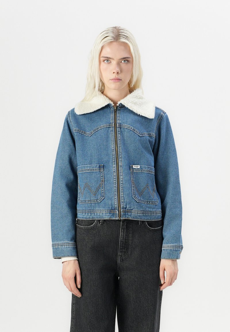 Světle modrá džínová bunda s krémovým kožešinovým límcem, zipovým zapínáním, dvěma náprsními kapsami a kontrastními švy. Unisex styl a zkrácený střih.