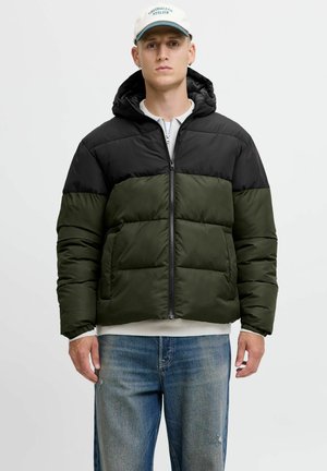 Pufferjacke met een zwart bovenstuk en een donkergroen onderstuk, gemaakt van een glanzende stof met een rits aan de voorkant en een capuchon. Draagt over een witte top.