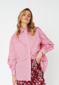 Pink and white striped button-up shirt with a pocket and ruffled sleeves, paired with a floral embroidered burgundy skirt.