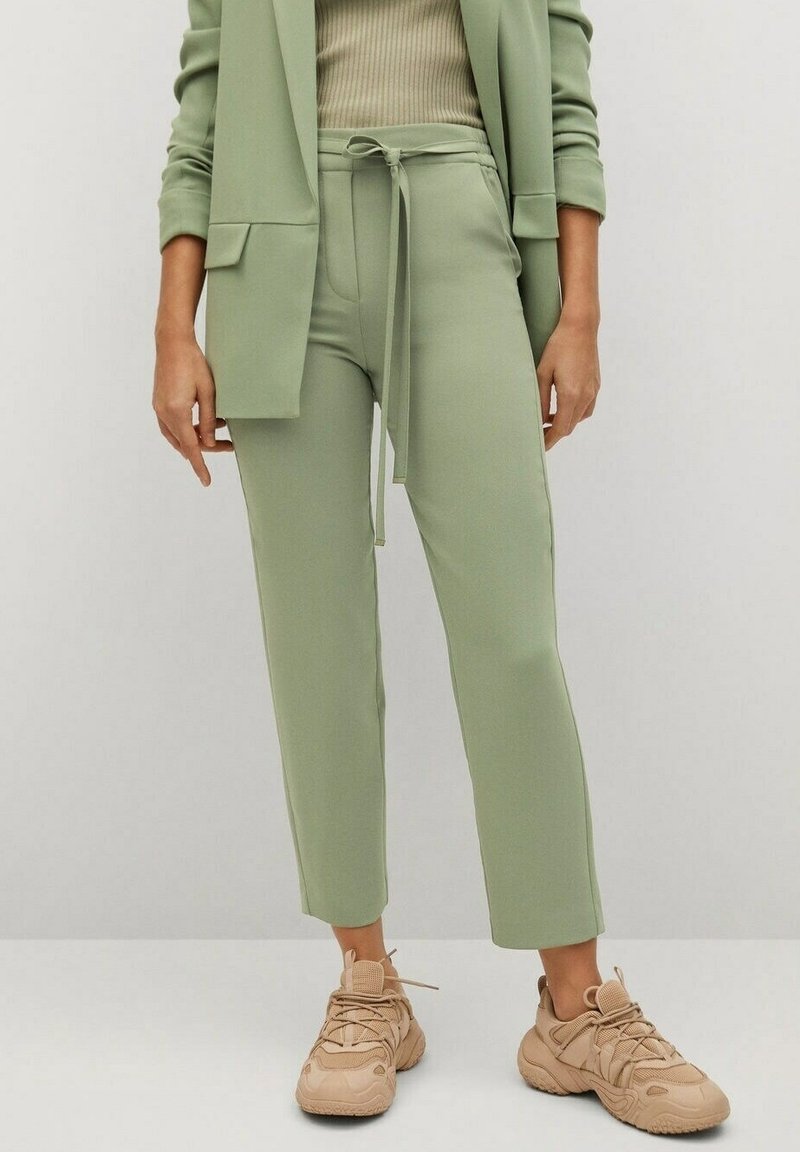 Pantalon vert clair avec taille à cordon, associé à un haut beige ajusté et des baskets beiges. Tissu doux, coupe droite.