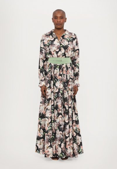 Rochie maxi florală cu un fundal negru, având flori mari roz și albe, mâneci lungi și o brățară verde deschis la talie.