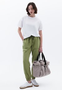 Camiseta blanca de manga corta, joggers verdes con cintura elástica y bolsillos, bolso de tela gris y zapatillas blancas con acentos grises.