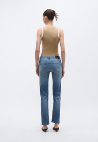 Beżowy prążkowany top na ramiączkach z białymi szelkami, zestawiony z jasnoniebieskimi jeansami o prostych nogawkach. Charakterystyczne tylne kieszenie oraz brązowa skórzana metka na pasku.