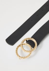 Zwarte leren riem met een gladde textuur, voorzien van een dubbele gedraaide gouden metalen gesp. Verstelbare maat met meerdere gaten.