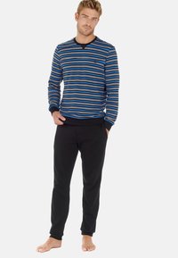 Stribet langærmet bluse i blå, sort og hvid, parret med sorte bukser. Blødt stof, rund hals, ribbede manchetter og smalle ankler.