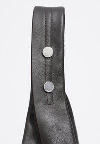 Tmavohnedý kožený remienok so hladkým povrchom, ktorý má dva strieborné kovové zapínania a kontrastné hnedé prešitie pozdĺž okraja.