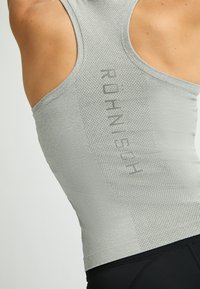 Camiseta atlética de color gris claro con textura de malla y logo en la parte posterior. Diseñada con un estilo de espalda nadadora y silueta ajustada.