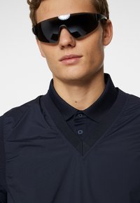 Marinblå pikétröja med v-ringning, i en strukturerad väv och med en tvåknappsstängning. Bärs tillsammans med stora svarta solglasögon med rund design.