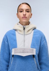 Blue fleece jacket with gray panel and beige collar, featuring a front zipper, two side pockets, and a logo patch on the chest.