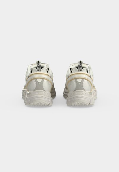Paire de chaussures de sport blanches vues de dos avec semelles texturées et languettes noires et blanches sur un fond uni.