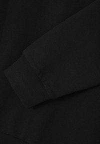 Un tessuto di felpa nera che presenta una texture liscia. Il polsino è caratterizzato da dettagli a coste, che migliorano la vestibilità e la struttura. Bordo senza cuciture.