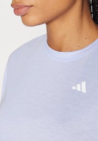 Heled lilla lühikese varrukaga särk ümmarguse kaelusega, mille vasakul rinnal on valge kolmnurga logo. Pehme tekstuur.
