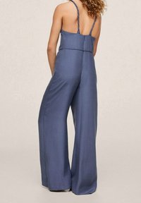 Mono azul con diseño sin espalda, tirantes delgados trenzados, piernas anchas y una textura de tela suave. Corte entallado desde la cintura hasta la cadera.