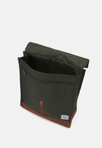 Zielona torba torebka z płótna z brązowym skórzanym dnem, z zamykaną na zamek przednią kieszenią oraz zapięciem na guzik, z fałdowanym klapowym wzornictwem.