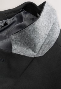 Cuello de abrigo negro con forro interior de lana gris y satén negro liso con patrón en el interior, mostrando texturas detalladas de la tela y costuras.