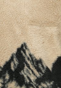 Beiger Fleece-Stoff mit einer weichen, strukturierten Oberfläche, die ein schwarzes Bergmuster zeigt, das organische Formen vor einem neutralen Hintergrund kombiniert.