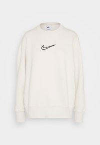 Krämfärgad sweatshirt med rund hals, ribbade muddarna och nederkant. Har en svart Nike-logotyp broderad på bröstet. Mjuk tygstruktur.